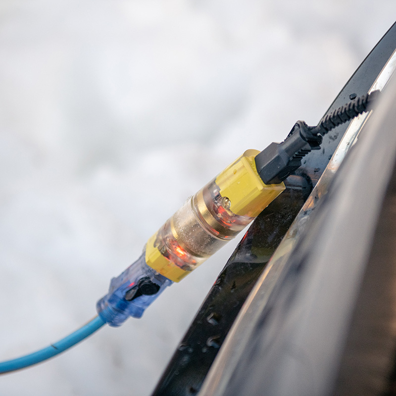 The Q-Plug hanging from a vehicle's block heater cord plugged into an electrical cord